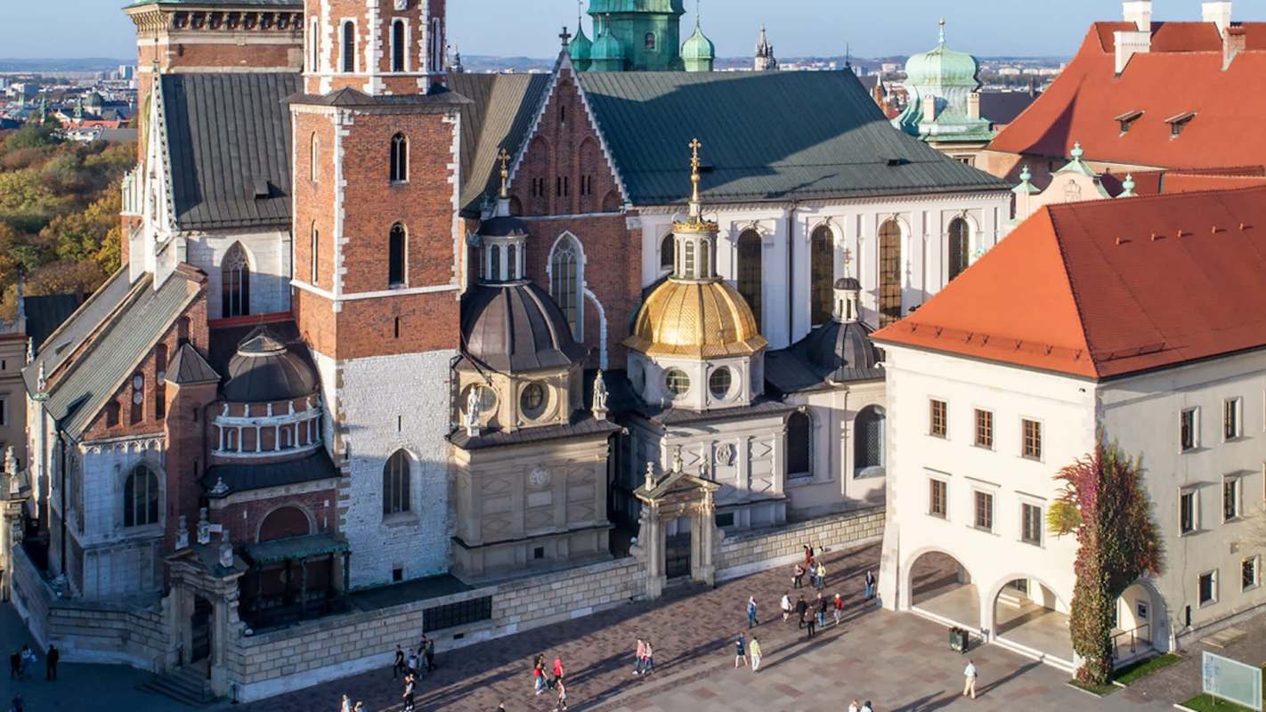 An aerial view of a historic building complex featuring domed roofs and a bustling square with people.