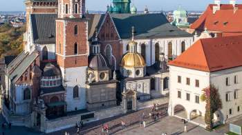 An aerial view of a historic building complex featuring domed roofs and a bustling square with people.
