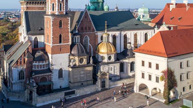 An aerial view of a historic building complex featuring domed roofs and a bustling square with people.