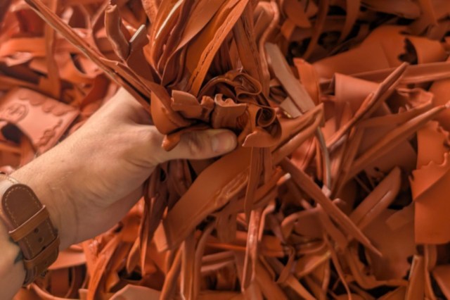 A hand grips a bundle of rubber scraps among a heap of similar material.