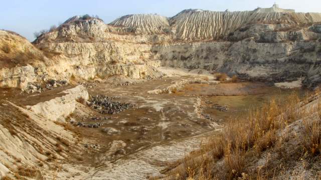 A barren, eroded sand quarry with steep, layered hills and sparse vegetation.