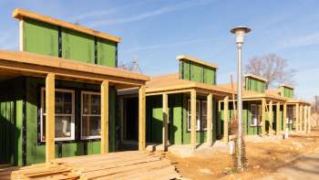 A row of new construction tiny houses with green siding and wooden supports under clear blue skies.