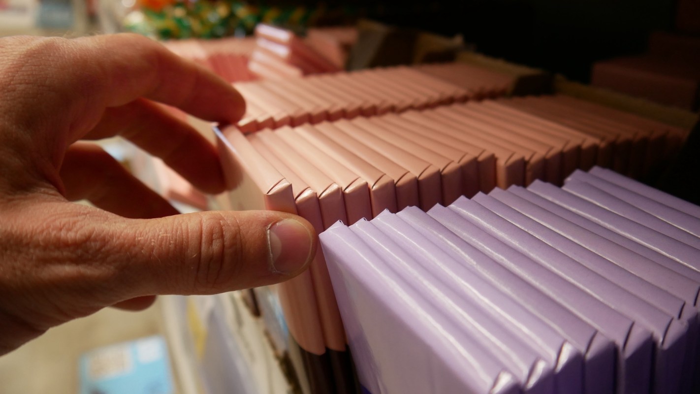 A hand reaches toward neatly stacked chocolate bar packages on a shelf.