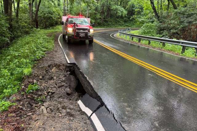 A red emergency vehicle parked near a cracked road edge surrounded by dense greenery on a rainy day.