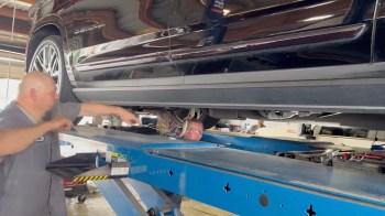 A mechanic points at a vehicle's undercarriage while another technician works underneath an elevated car.