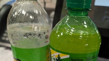 A clear plastic bottle of sparkling water next to a green sports drink bottle with a green cap.