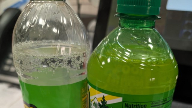 A clear plastic bottle of sparkling water next to a green sports drink bottle with a green cap.
