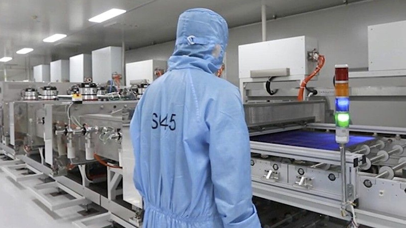 A worker in a blue coverall operates machinery in a cleanroom.