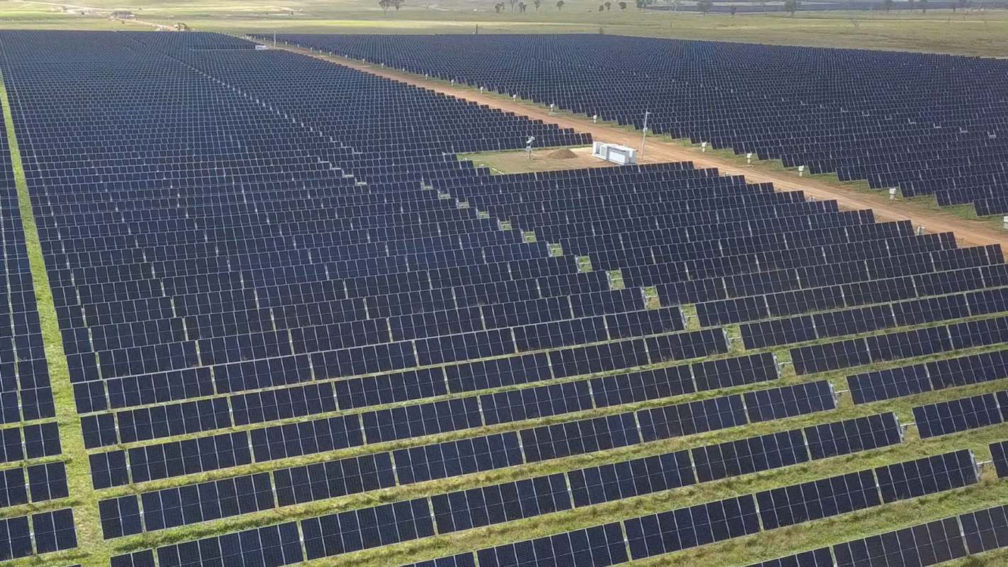 Aerial view of a vast solar farm with rows of solar panels and a service area in the center.