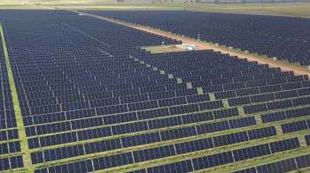 Aerial view of a vast solar farm with rows of solar panels and a service area in the center.
