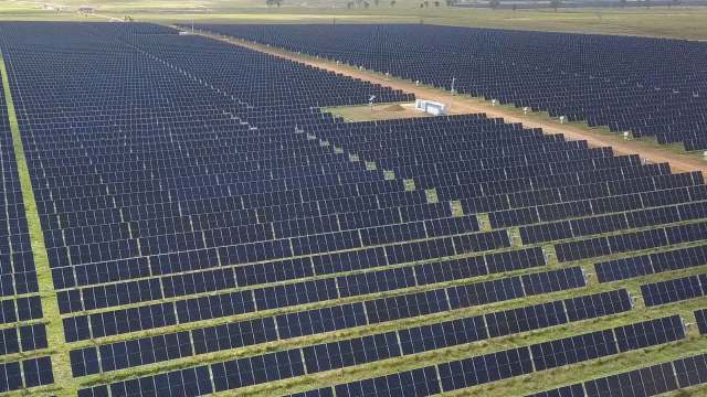 Aerial view of a vast solar farm with rows of solar panels and a service area in the center.