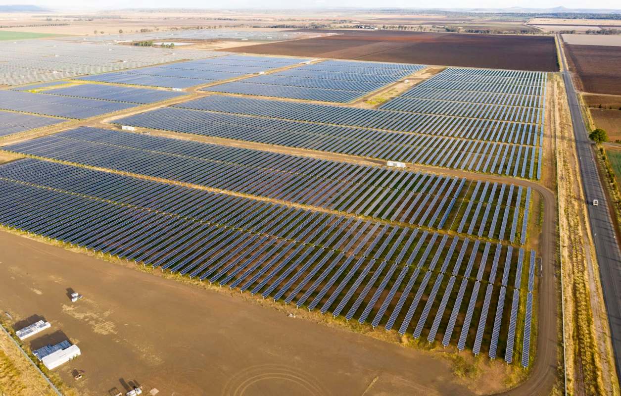 Aerial view of a large solar farm with rows of solar panels under a clear sky.