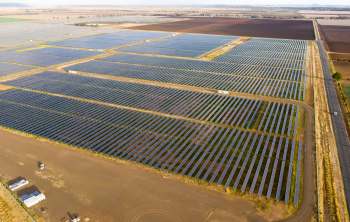 Aerial view of a large solar farm with rows of solar panels under a clear sky.
