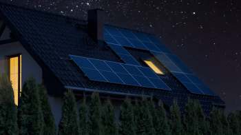 A house with solar panels on the roof is illuminated under a starry night sky.
