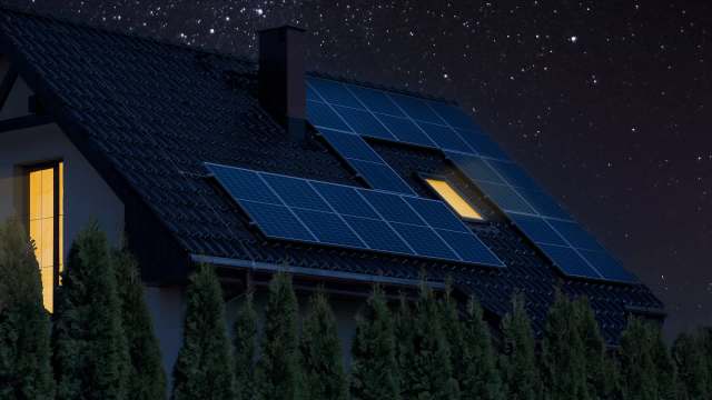 A house with solar panels on the roof is illuminated under a starry night sky.