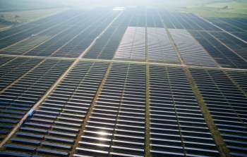 Aerial view of a large solar panel field with rows of panels and a few service vehicles.