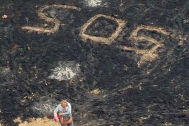 A person stands on blackened ground, with "SOS" written in large letters nearby.