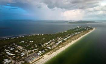 An aerial view of a coastal area featuring houses, sand, and water as storm clouds approach.