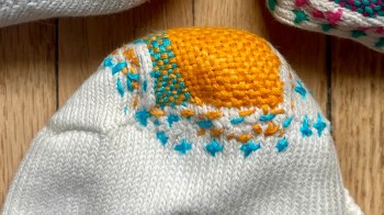 A close-up of a white sock with colorful embroidery, featuring orange and blue stitching.