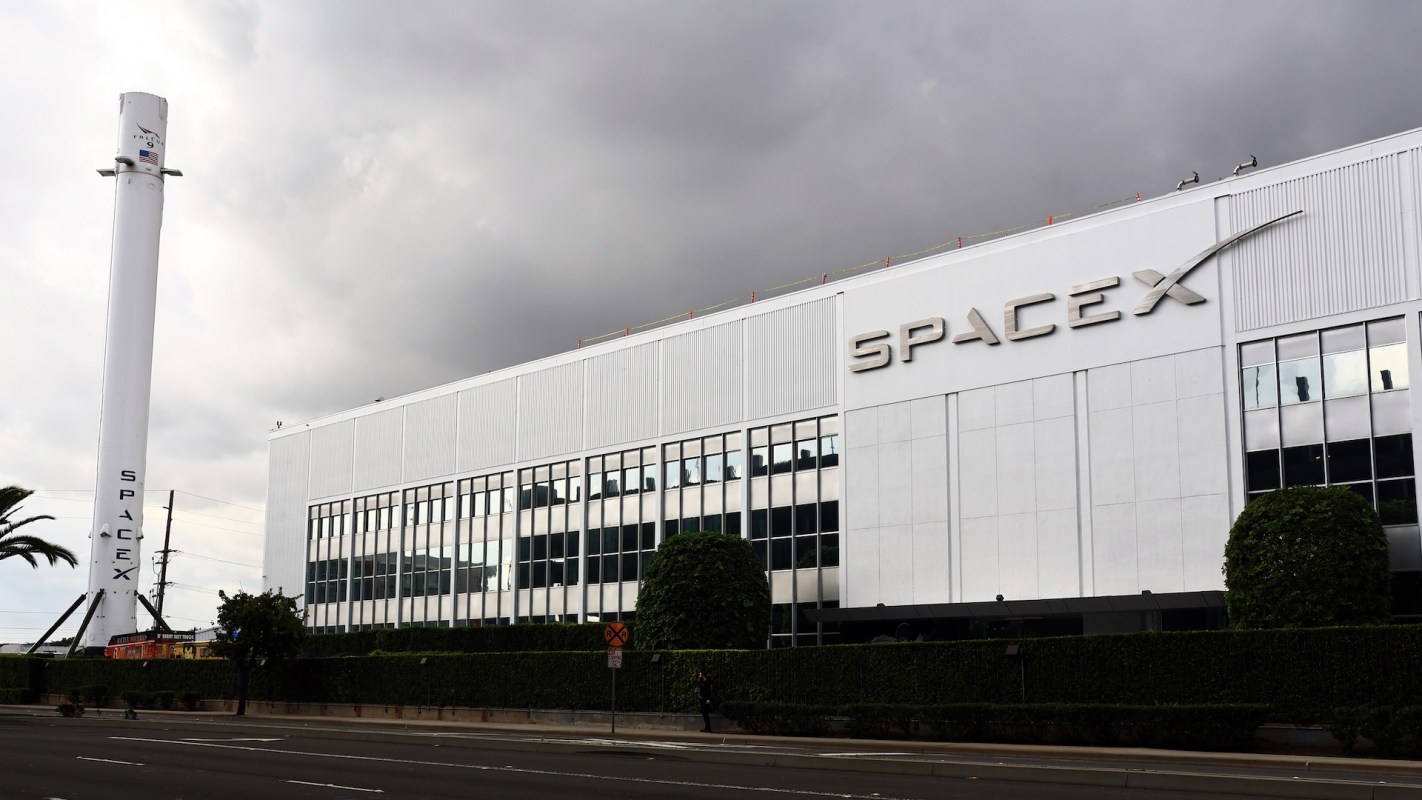 A SpaceX facility featuring a rocket display and modern architecture under a cloudy sky.