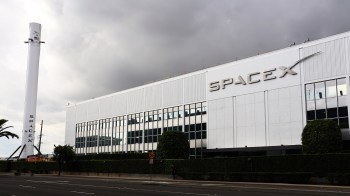 A SpaceX facility featuring a rocket display and modern architecture under a cloudy sky.
