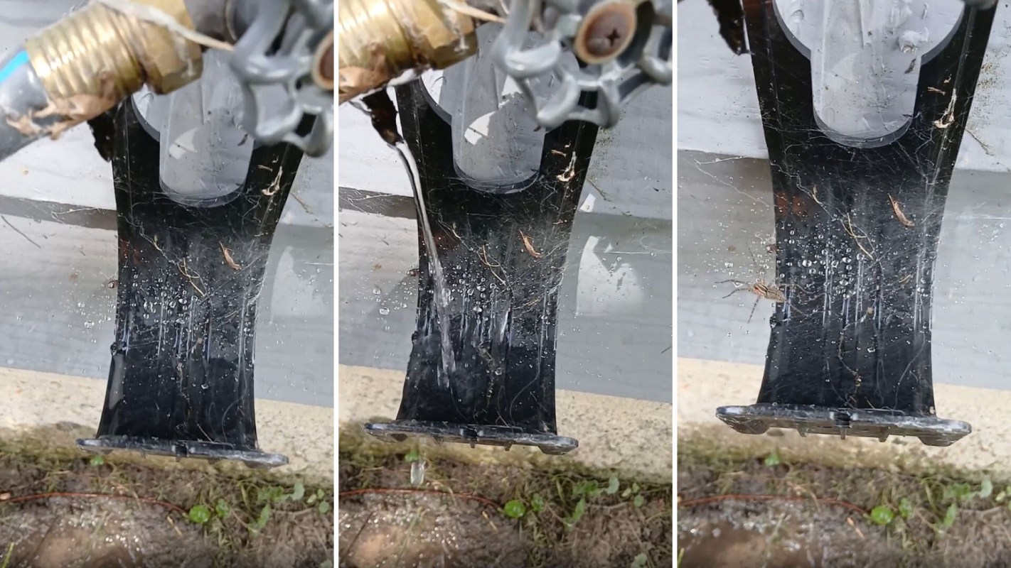 Water pours from a faucet spout onto a surface covered with dirt and spider webs.