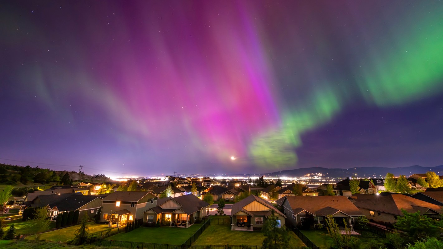 A vibrant aurora borealis lights up the night sky over a suburban neighborhood.