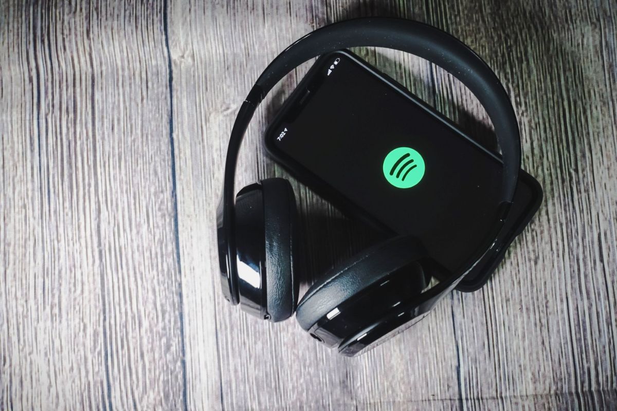 Headphones on a phone displaying the Spotify logo.