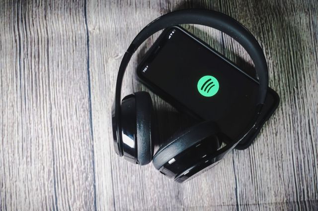 Headphones on a phone displaying the Spotify logo.