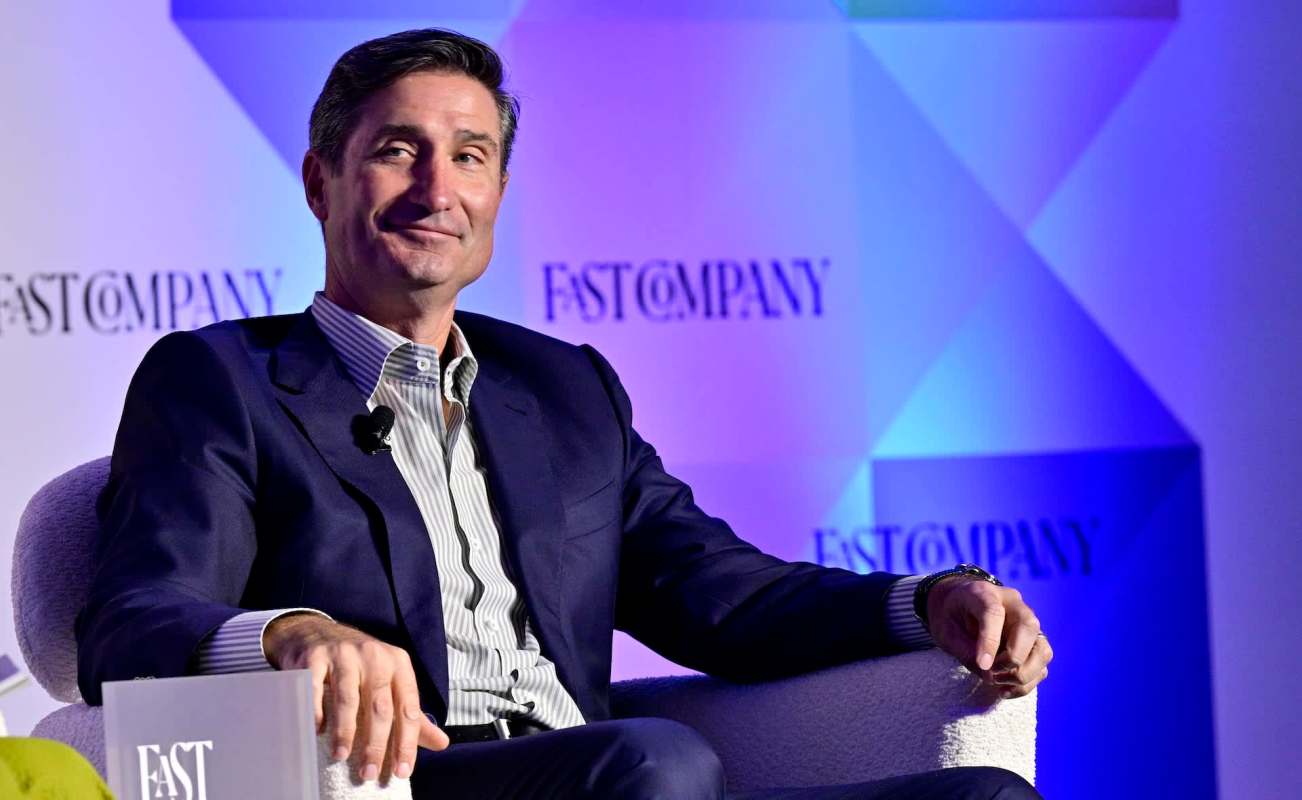 Starbucks CEO Brian Niccol smiles in a suit while sitting on a stage with a backdrop that reads "FAST COMPANY."
