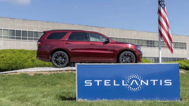 A red SUV parked near a Stellantis sign, with a U.S. flag and a modern building in the background.