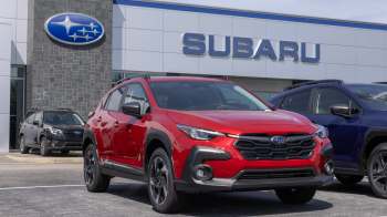 A red Subaru SUV parked outside a dealership with a Subaru logo and additional cars in the background.