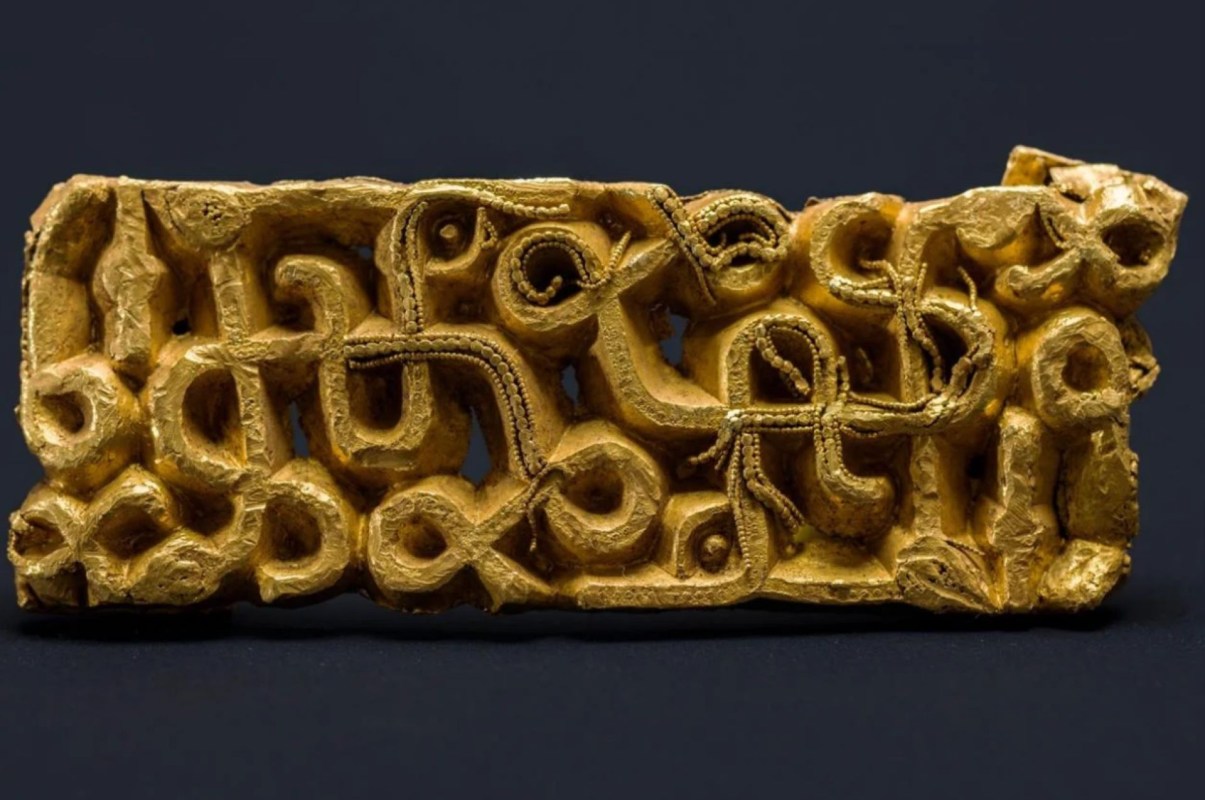 A decorative gold artifact featuring intricate, abstract patterns and shapes against a black background.