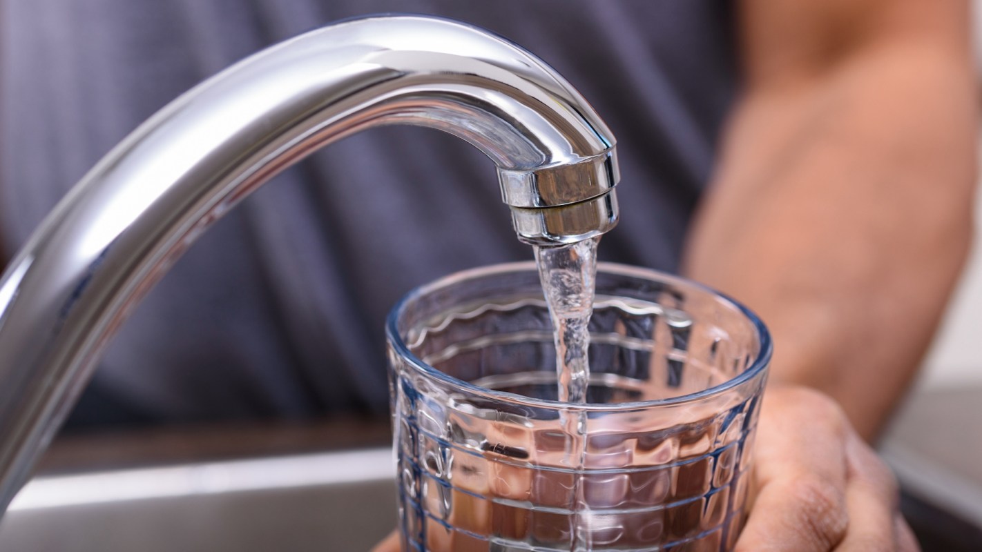 A close-up of a chrome faucet pouring water into a clear glass held by a person's hand.