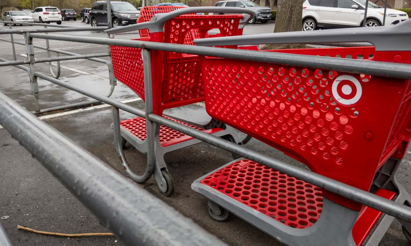 Two red Target shopping carts are lined up in a parking lot, partially visible behind a metal railing.