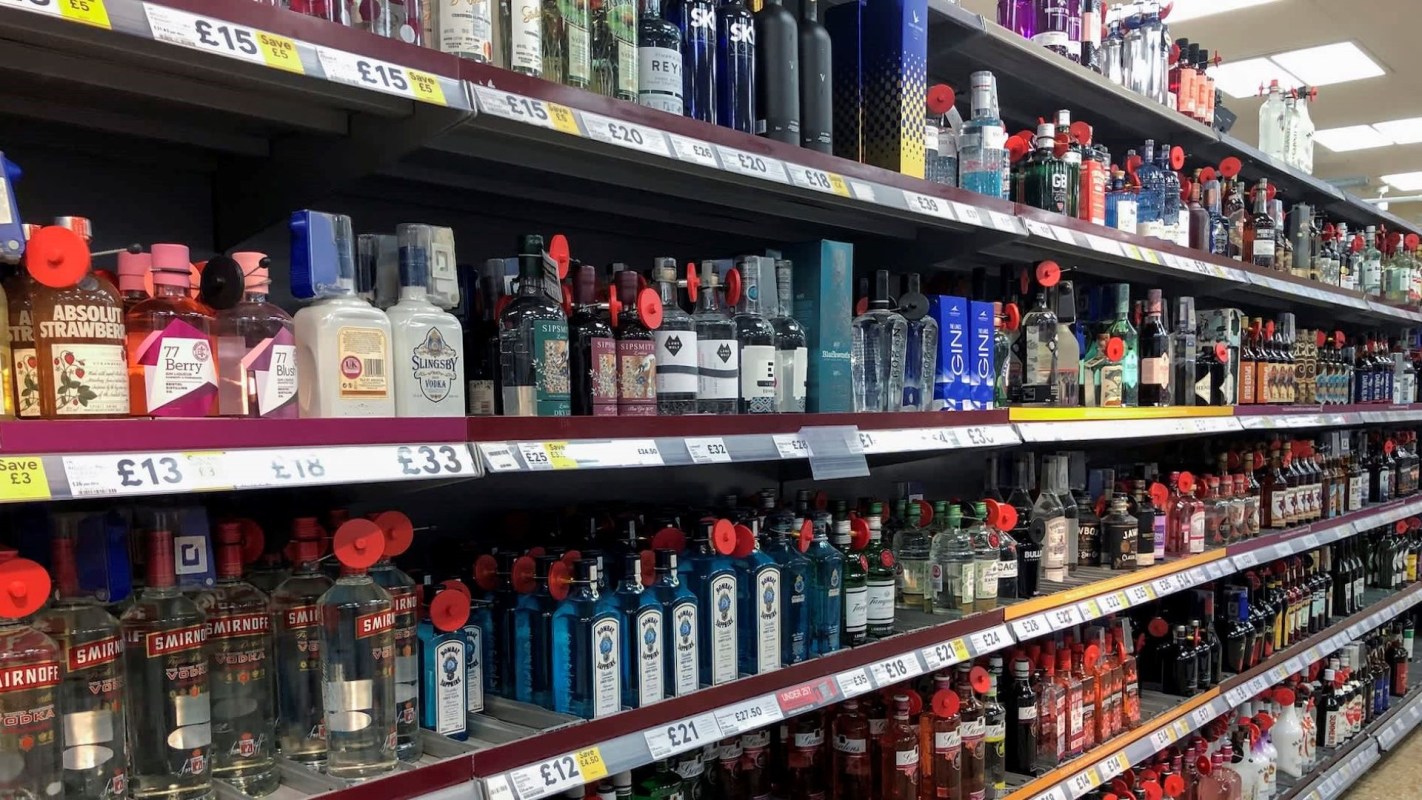 A supermarket shelf displays various bottles of liquor, priced and tagged for purchase.