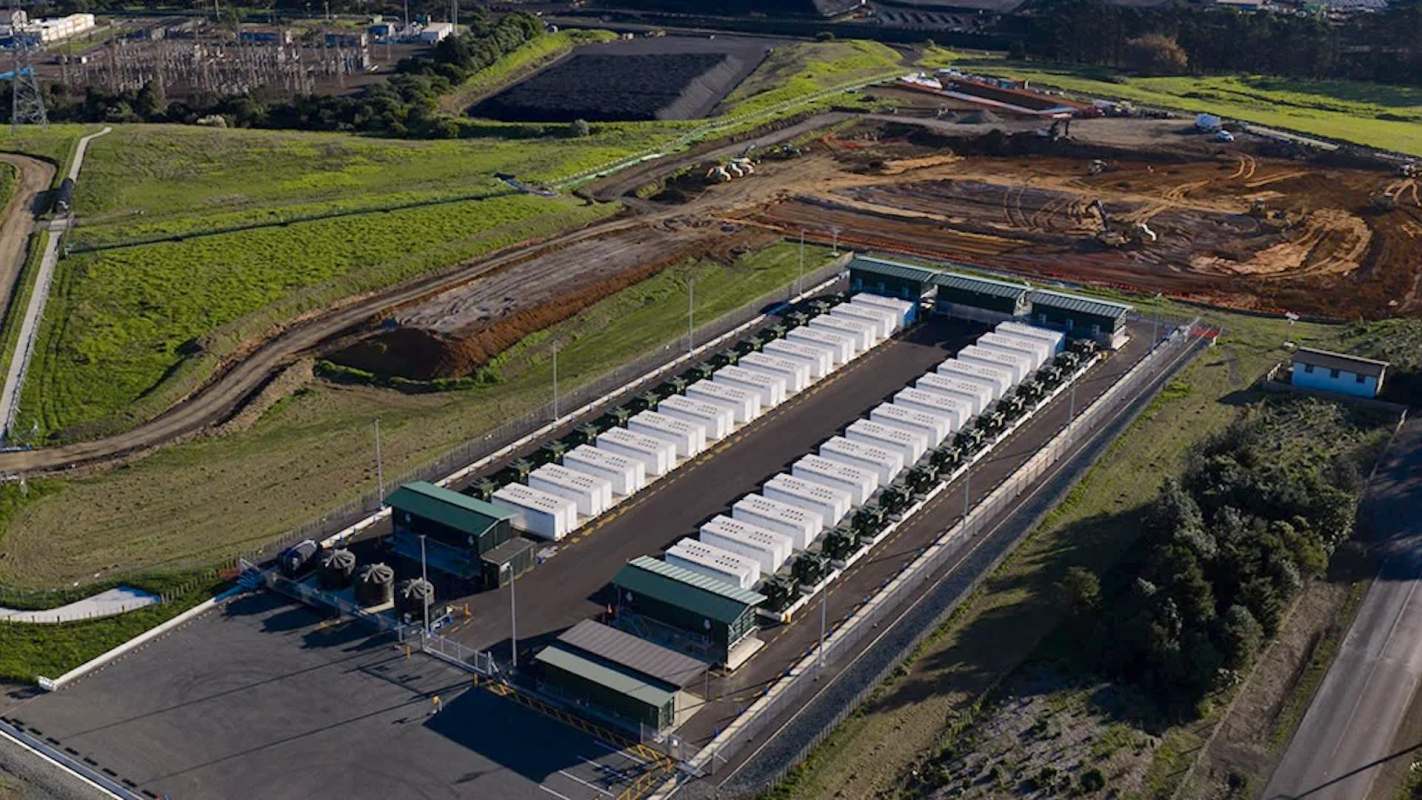 An aerial view of a battery storage facility surrounded by green fields and construction.