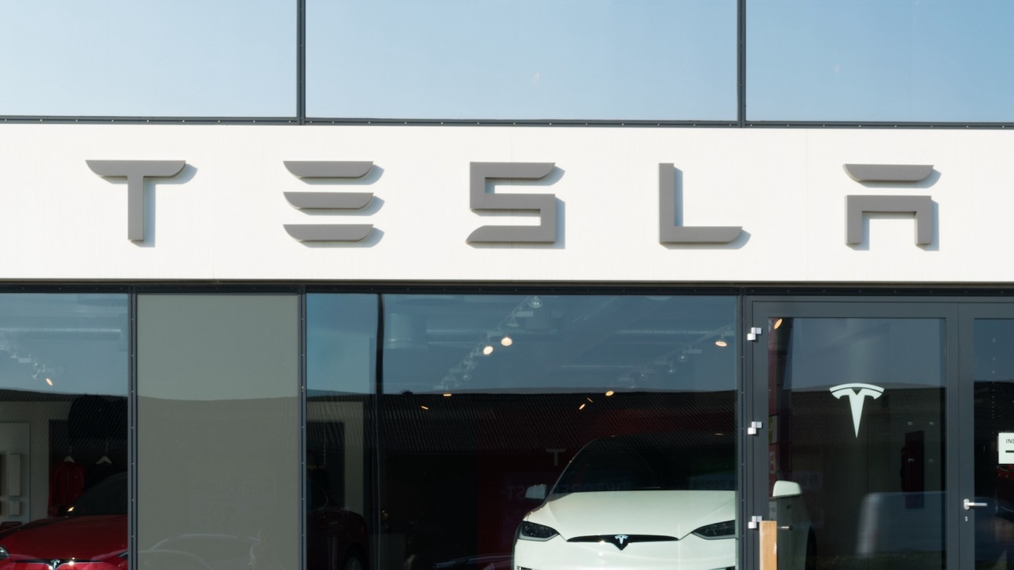 A Tesla dealership featuring the brand's logo and a white electric vehicle on display.