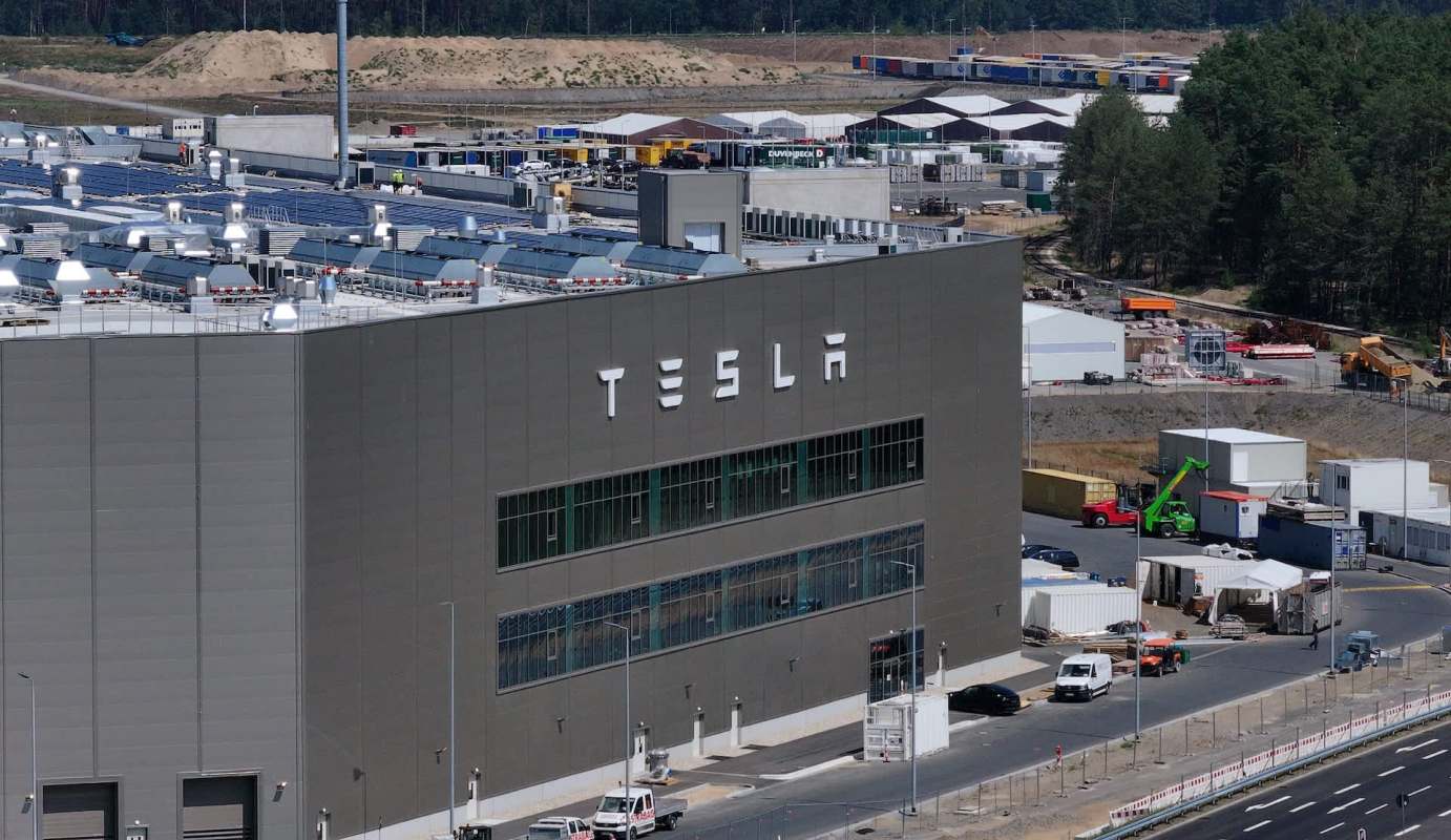 A Tesla factory building in Berlin with solar panels on the roof, surrounded by construction and storage areas.