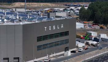 A Tesla factory building in Berlin with solar panels on the roof, surrounded by construction and storage areas.