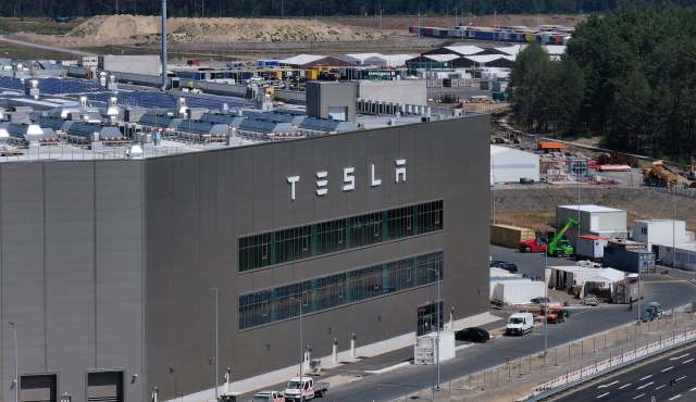 A Tesla factory building in Berlin with solar panels on the roof, surrounded by construction and storage areas.