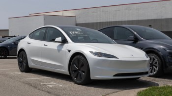 A white Tesla sedan parked in a lot with a gray Tesla SUV in the background.