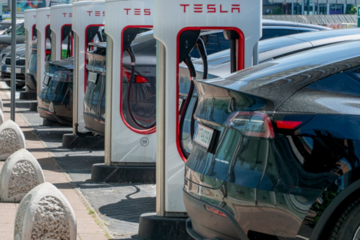 A row of Tesla charging stations with black cars parked nearby on a sunny day.