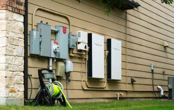 Two Tesla Powerwall units mounted on a house wall, alongside electrical meters and pipes.