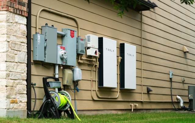 Two Tesla Powerwall units mounted on a house wall, alongside electrical meters and pipes.