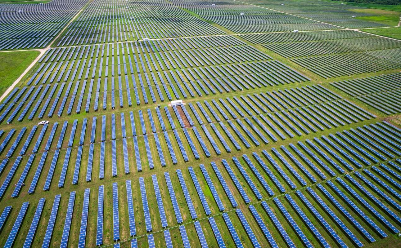 An expansive solar farm with rows of solar panels on a green field.