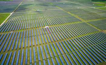An expansive solar farm with rows of solar panels on a green field.