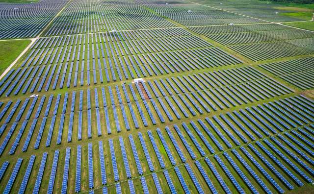 An expansive solar farm with rows of solar panels on a green field.