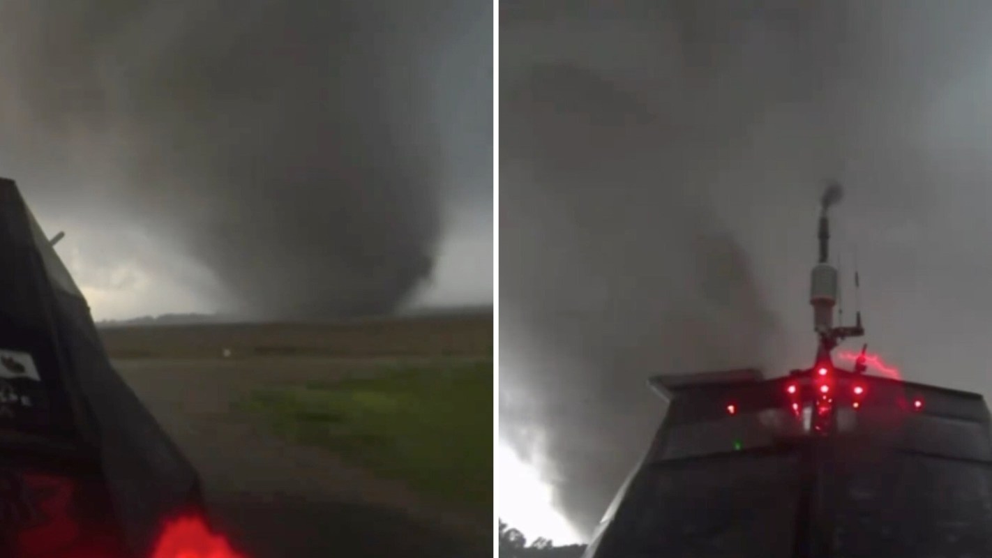 A tornado looms ominously in the distance, viewed from a vehicle's perspective.