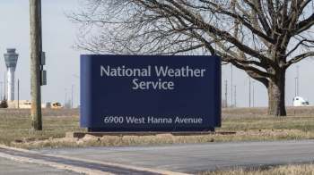 A sign for the National Weather Service, located at 6900 West Hanna Avenue, with an airport control tower visible in the background.